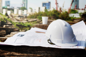 A white construction helmet and documents, with a construction site visible in the background